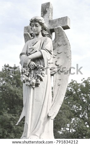 View of statue of an angel against dark foliage background. Dramatic unusual scene of statue angel as a symbol of the end of life and afterlife.