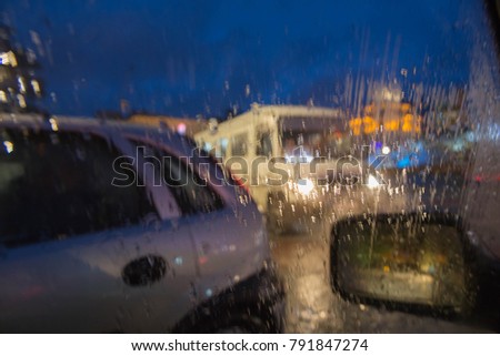 Rain drops on car glass, Night. Rain drops on window, rainy weather, rain background. Blurry car and bus silhouette