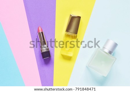 Pink lipstick, yellow bottle of female perfume, blue bottle of toilet water on a colorful background. Flat lay stock beauty photography. Image for beauty blog