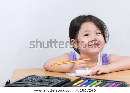 The girl with a pencil and a dress on the table in a lovely purple dress. Smile with the camera while drawing fun. with space for text.

