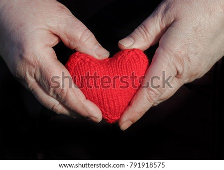 old man with wrinkled hands with fingers knitted red heart