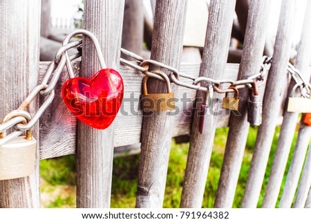 Happy Saint Valentines day card background. Lovely heart shaped bright red locked up love padlock on strong old rusty steel chain hanging on grunge grey wooden fence around fresh green spring garden.