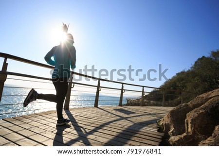 sporty female runner running on seaside boardwalk during sunrise