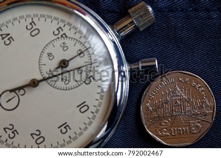 Thai coin with a denomination of five baht and stopwatch on old worn blue denim backdrop - business background