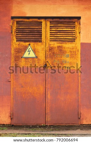 Old metal rusty grunge door to electric switchboard with high voltage arrow lightning sign in yellow triangle, abstract background