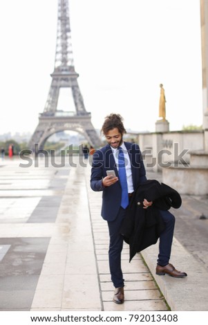 Happy young boy having fun and talking with friend with smartphone near Eiffel Tower in background. Gladden man enjoying with travelling France and visiting famous places. Concept of cheap calls and