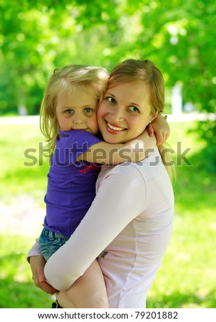 Mum holds the small daughter outdoors smiling