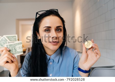 young brunette girl in blue shirt holds in hands golden bitcoin and dollars