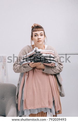 surprised girl holding stack of clothes on hangers and looking at camera