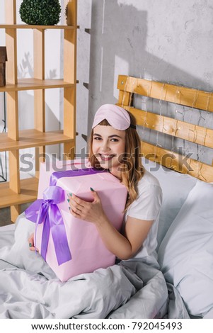happy girl sitting in bed with present box and looking at camera