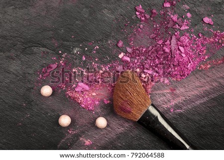 A closeup of a makeup brush with vibrant pink and purple eye shadow, shot from above on a black texture with copy space