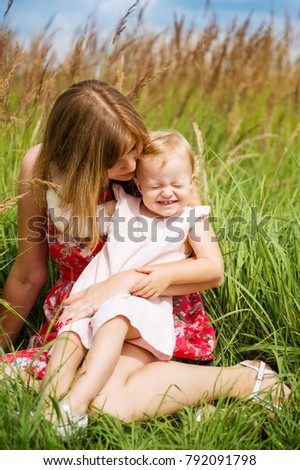 Mother and child girl playing, kissing and hugging in green field. Happy mother's day. Spring family holiday concept