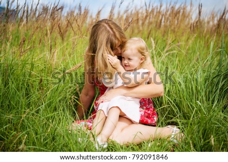 Mother and child girl playing, kissing and hugging in green field. Happy mother's day. Spring family holiday concept