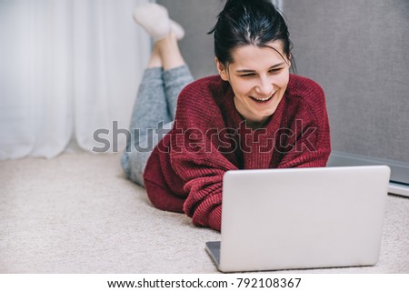 Happy young woman talking with friend using wireless. Casual female smiling and lying on the carpet while browsing online shopping website using notebook. People and lifestyle concept