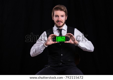 Man in suit holding phone with green screen on black background 