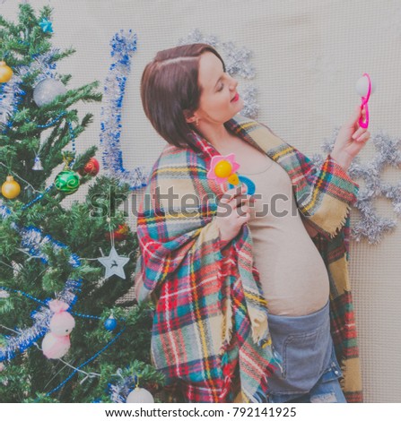 pregnant girl near the Christmas tree with a rattle in his hand