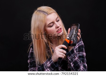 Aggressive girl, cuts the screen of broken smartphones using a construction knife. Black background.