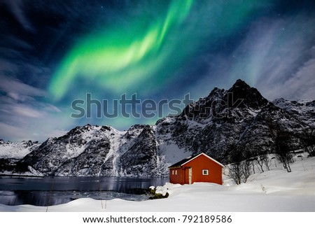 Lofoten Islands, Svolvaer, Northern Lights over a frozen lake and red rorbu, Norway. Royalty-Free Stock Photo #792189586