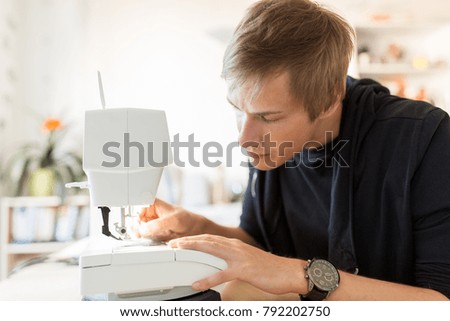 people, clothing and tailoring concept - fashion designer threading up sewing machine needle at studio
