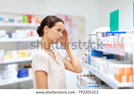 medicine, pharmaceutics, healthcare and people concept - female customer having headache choosing drugs at pharmacy Royalty-Free Stock Photo #792205312