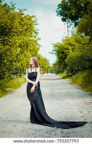 portrait of a girl. in a black dress with a train. on a background of a bush with roses.