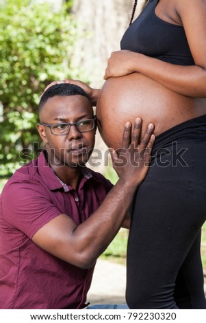 African-American man with his ear on the belly of his pregnant wife
