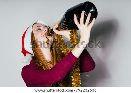 sweet red-haired girl with a red cap like Santa Claus celebrates the new year 2018, drinks champagne from the bottle