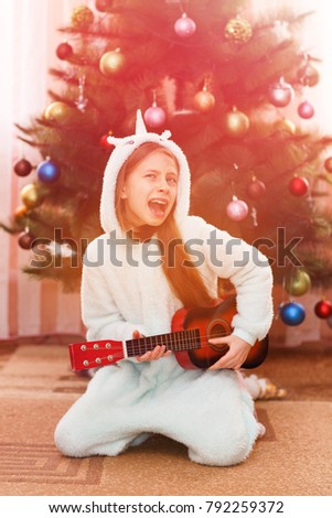 Child  playing the guitar and singing near a christmas tree.