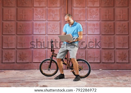 Bmx rider posing on bike otdoors and looking at laptop