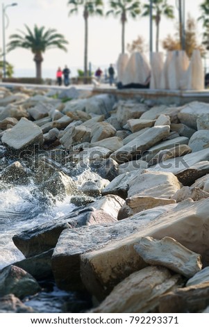 Photo of sea shore, stones, palms and tourists