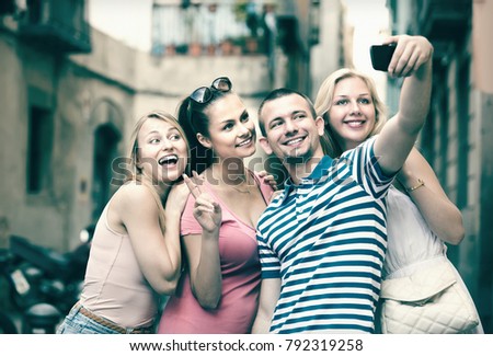 Four cheerful smiling friends taking self portrait with mobile phone in town