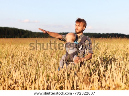 father shows his son (infant baby in sling) a field of barley, Russia