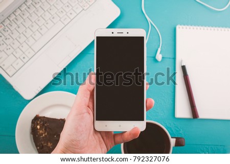 hand of a girl with a phone, desktop with a laptop, space for text