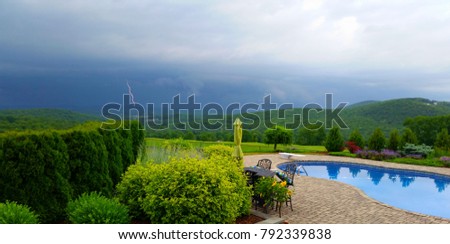 Lightning Bolt Captured in Stormy Summer Sky Near In-Ground Swimming Pool and Patio, Lush Greenery in Foreground; Safety First, Weather, Travel and Wealth Concepts