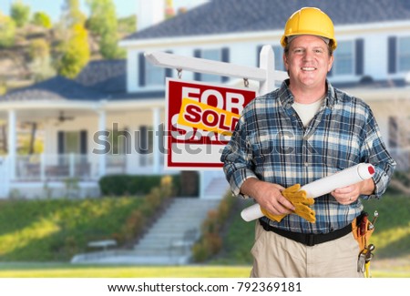 Contractor With Plans and Hard Hat In Front of Sold For Sale Real Estate Sign and House.