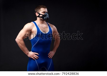 A young dark-haired man fighting Greco-Roman wrestling in a blue wrestling tights  and training mask  posing against  a black isolated background