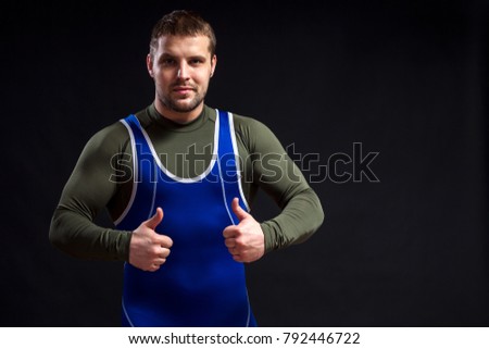 Young adult man wrestler  in a blue   tights  shows thumbs up on a black isolated  background