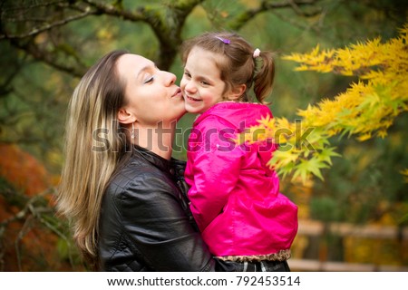 Happy family concept. Fall in Portland Japanese Park in Oregon USA. Mother Hugging and Kissing Little Girl Child Daughter. Colorful Background