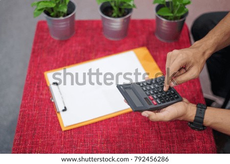 Man hand holding a calculator and pen on white note pad.Man using calculator on a wooden table with note pad and pen.