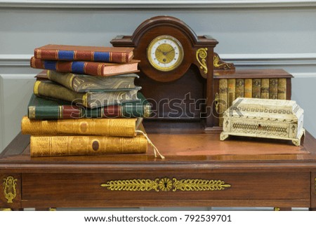 A stack of old books on an antique table with a clock, and a carved casket.