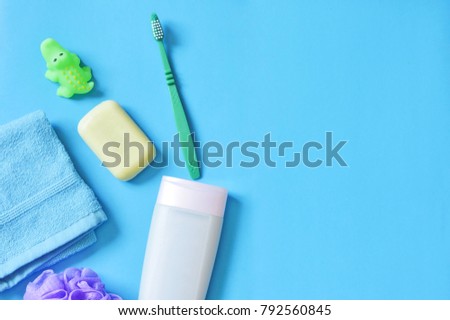 Blue terry towel, purple sponge, baby soap, green rubber toy crocodile and shampoo bottle on a blue background. Flat lay bath products. Mock-up, free space for text. Stock beauty photo