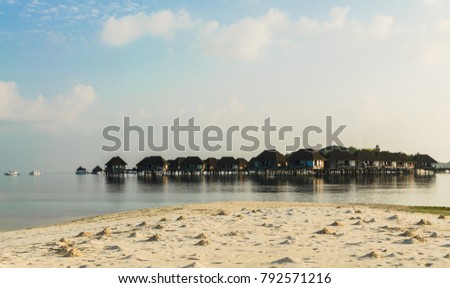 In foreground: beach with sandy hills made by crabs, in background: beautiful wooden villas, standing on stilts in water of Indian Ocean, sunrise, Maldives. Travel and tourism concept