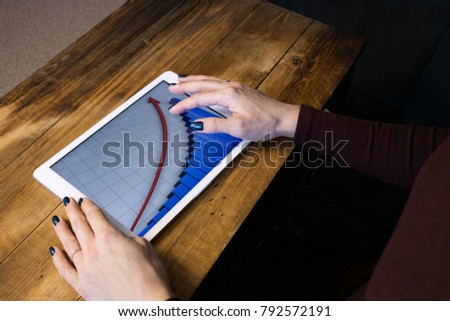 The girl working with a tablet computer. The graph rises. Table, wooden, background black.