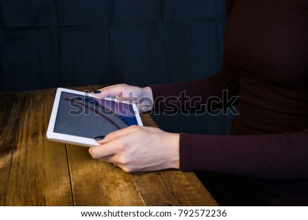 The girl working with a tablet computer. The graph rises. Table, wooden, background black.