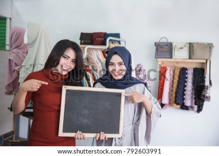 portrait of two asian fashion store owner smiling while holding blank board sign in her shop
