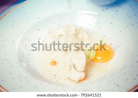 Broth with dumplings iand an egg yolk being poured from a jug