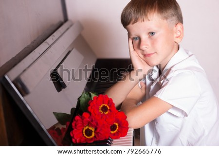 A young pianist sits at the piano with a bouquet of red flowers. A recital of classical music. Having propped his head with his hand tired after the musical performance of the encore.