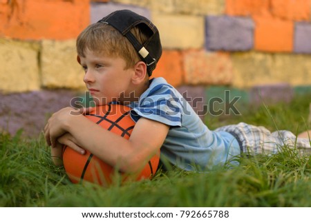 The guy with the ball lies on a natural grass cover. I put my head on the basketball. He pressed the ball with both hands. Playground for children for basketball.