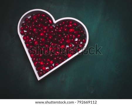 Simple composition with red  berries in a heart shape representing on the blue rough wooden background.