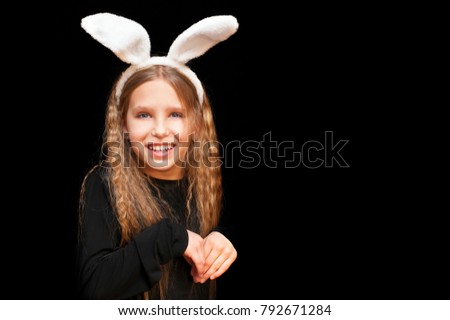 Young girl on a black background with ears of a hare on her head. She folded her hands like a hare. Easter hare